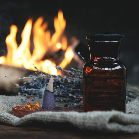 staged photo with incense cone, amber glass bottle on cloth with fire in background