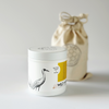 Minimal white candle container with lid featuring crane illustration and reusable linen bag packaging