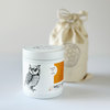 Minimal white candle container with lid featuring owl illustration and reusable linen bag packaging