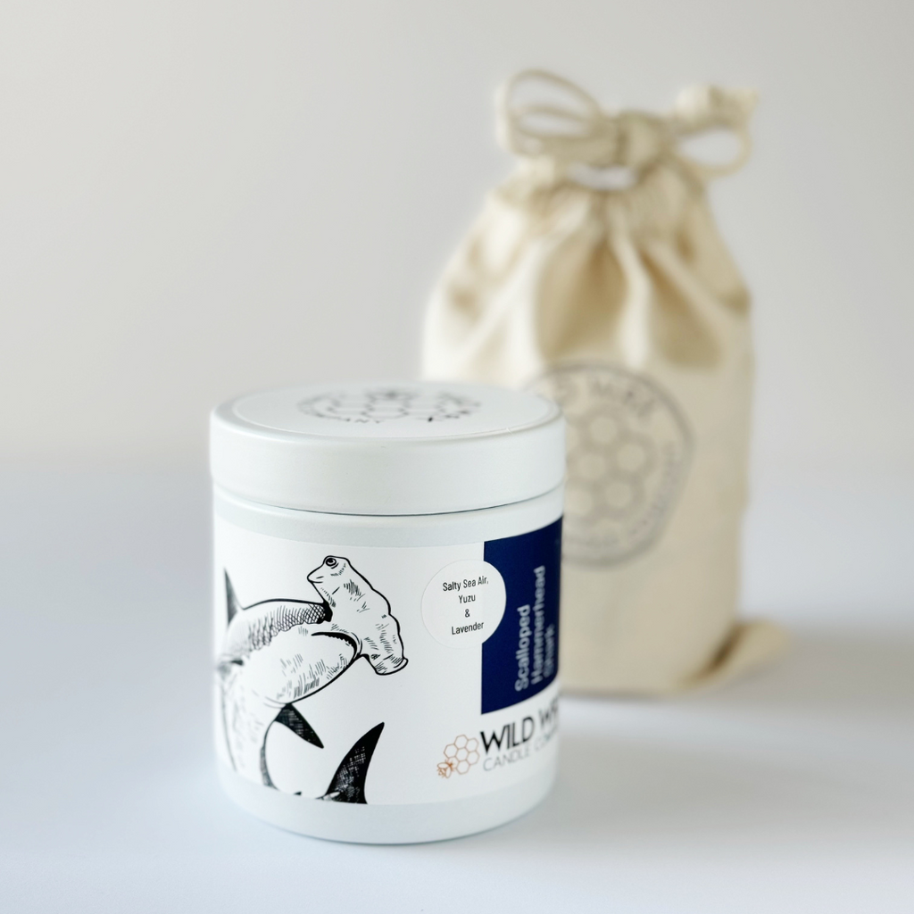Minimal white candle container with lid featuring shark illustration in front of linen drawstring gift bag 