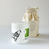 Minimal white candle container with lid featuring wolf illustration and reusable linen bag packaging