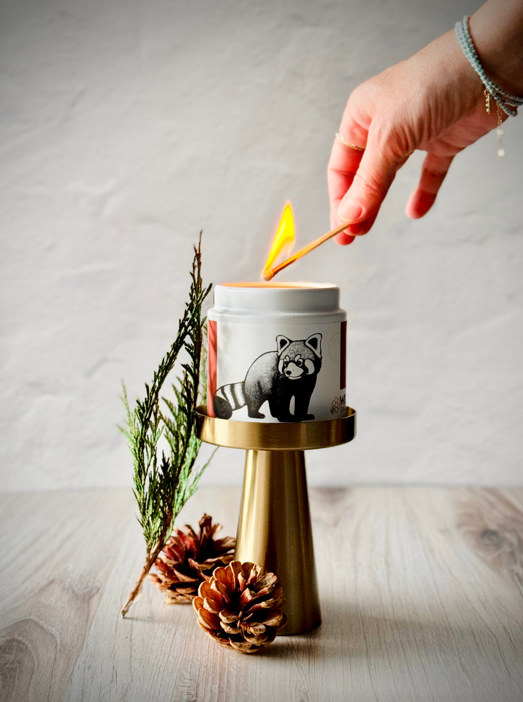 Hand lighting a candle with red panda design in a stylized scene