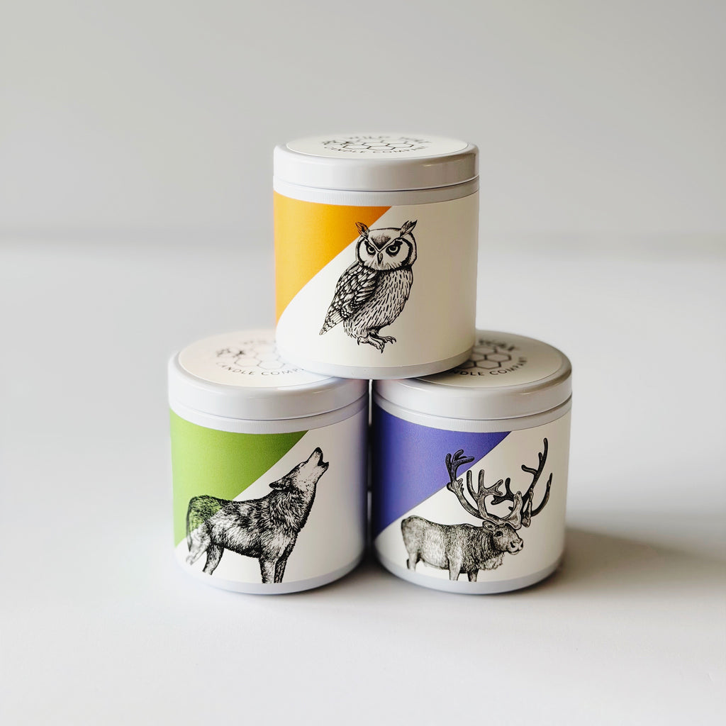 Three small container candles with lids and animal graphic designs of an owl, wolf, and caribou on the labels.